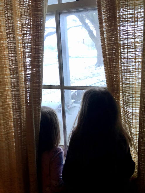 Sisters Avery and Marie Guidry spy snow through their living room window in Crowley, Louisiana, Monday, Feb. 15, 2021.